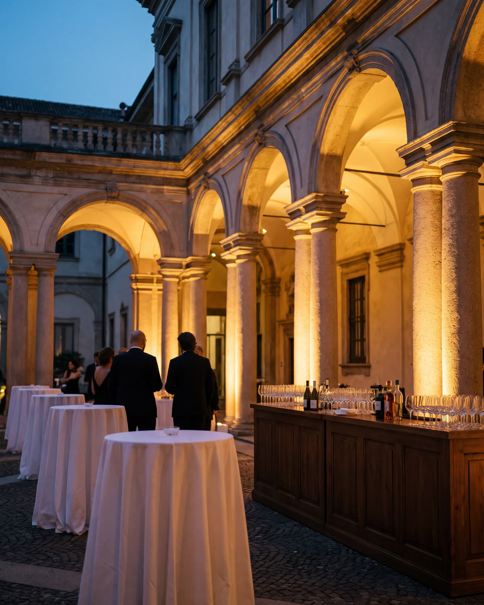 Il cortile porticato di un palazzo allestito per un cocktail aziendale, la sera.